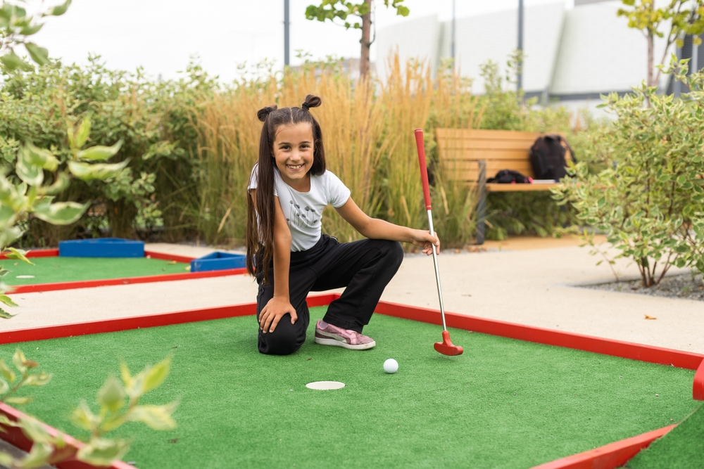 A happy young teen girl about to putt her golf ball in for a game-winning point
