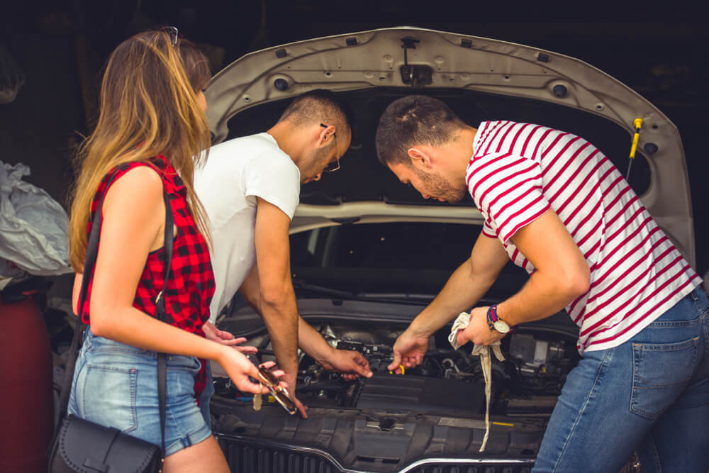 Three friends working on a car’s engine in their home garage.